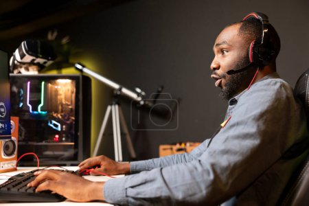 Hombre afroamericano usando auriculares mientras juega videojuegos en casa, mostrando emoción de asombro en la cara. Jugador en asombro mientras disfruta del juego en el ordenador, sorprendido por los gráficos de alta calidad