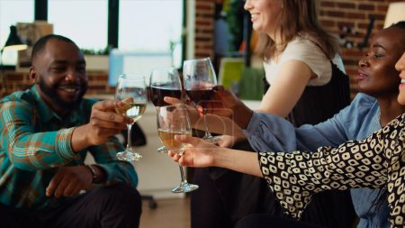 Téléchargez les photos : BIPOC groupe d'amis parlant entre eux dans le salon élégant appartement, réunis pour célébrer l'événement festif. Meilleurs amis socialiser à la maison, déguster du vin et des hors-d'œuvre - en image libre de droit