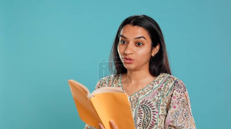 Radiant person reading interesting book, enjoying hobby, being entertained, isolated over studio background. Upbeat woman with novel in arms enjoying relaxation time, reading text aloud, camera B