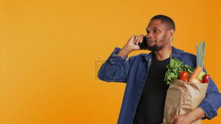 Ein afroamerikanischer Mann auf Einkaufstour im Supermarkt plaudert am Telefon und diskutiert mit Menschen über einen neuen Null-Müll-Ökomarkt in der Stadt. Junge Erwachsene empfehlen frische Bioprodukte. Kamera B.