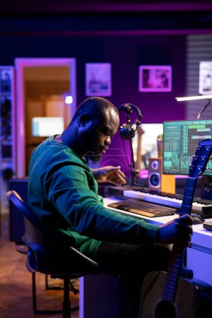 Artiste afro-américain jouant de la guitare et synthétiseur de piano électronique en home studio, enregistrement acoustique avec console de mixage pour produire des airs cool. Technicien du son édition de fichiers audio enregistrés.