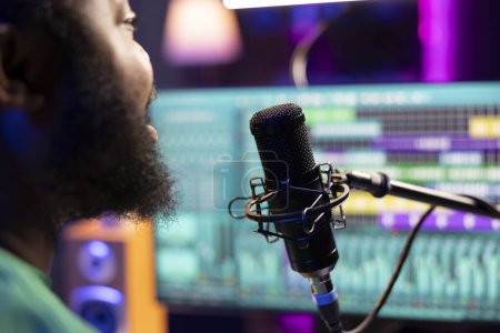 Compositeur masculin enregistrant sa mélodie sur microphone en home studio, chantant une chanson de sa propre création. Artiste talentueux utilisant ses fichiers audio et ses paroles pour appliquer des techniques de mixage et de mastering.