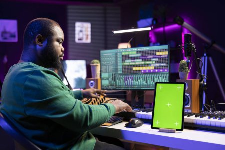 Audio technician composing new tracks with digital mix master software, having a tablet with isolated copyspace on desk. Professional engineer editing music in post production.