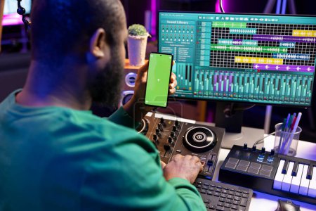 African american audio engineer recording and editing tracks with daw software, looks at greenscreen display. Young composer singer producing tunes for his new songs, home studio.