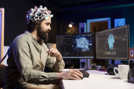 Man using EEG headset to communicate with artificial intelligence on computer in binary code. Programmer sending brainwave signals to AI entity on PC using high tech device