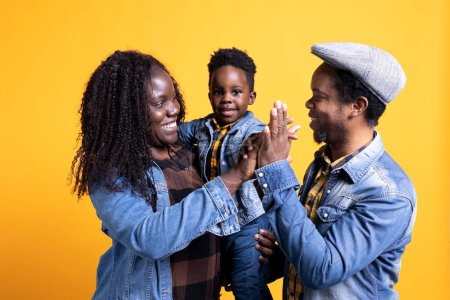 Glückliche schwarze Familie, die sich im Studio eine hohe Fünf teilt, fröhlich ist und Zuneigung zueinander zeigt. Afrikanisches Paar mit kleinem Kleinkind posiert mit Dankbarkeit.