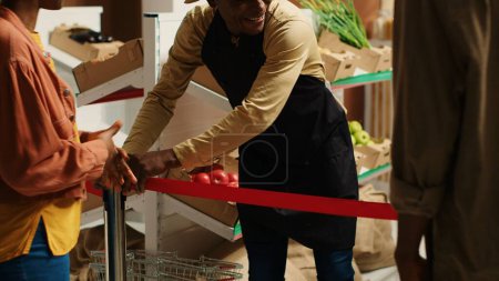 Der örtliche Händler öffnet die Türen des Lebensmittelgeschäfts und begrüßt die Kunden mit frischem Obst und Gemüse aus biologischem Anbau. Afrikanisch-amerikanischer Verkäufer, der umweltfreundliche Lebensmittel verkauft. Kamera 1.