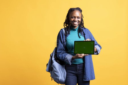 Glückliches afrikanisches amerikanisches Mädchen lacht, während es Tablet mit isoliertem Bildschirm und Studiohintergrund präsentiert. Fröhliche BIPOC-Person hat Spaß bei Promotion für Chroma-Schlüsselgerät