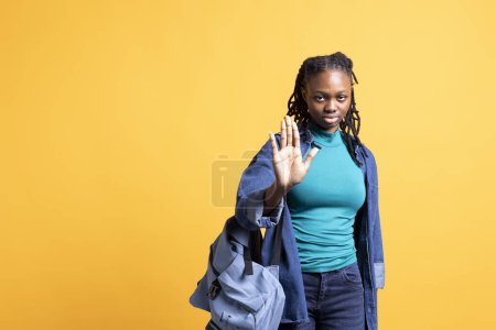 Selbstbewusste afrikanisch-amerikanische Frau macht Stop-Hand-Geste. Genervte BIPOC-Person gestikuliert mit festem Stoppschild, will Konzept beenden, isoliert über gelbem Studiohintergrund