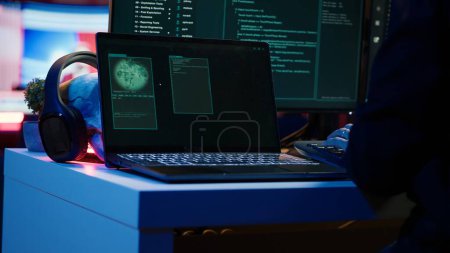 Kapuzenjungs nehmen Laptop aus dem Koffer und bereiten sich auf DDoS-Angriffe vor. Nahaufnahme von Betrüger am Computer Schreibtisch, der Notizbuch aus Tasche holt, Arbeit an Malware-Skript aufnimmt, Kamera A