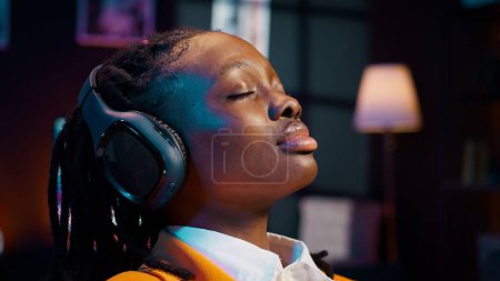 Unbekümmerter Student erstellt eine Präsentation und entspannt sich nach langer Recherche mit Musik auf dem Audio-Headset. Afroamerikanische Mädchen chillen mit Ambiente-Melodien. Kamera B.