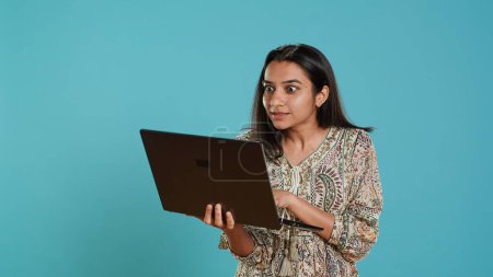 Upbeat woman saluting coworkers, having friendly conversations during teleconference meeting using laptop, studio background. Person discussing during online videocall on notebook device, camera A