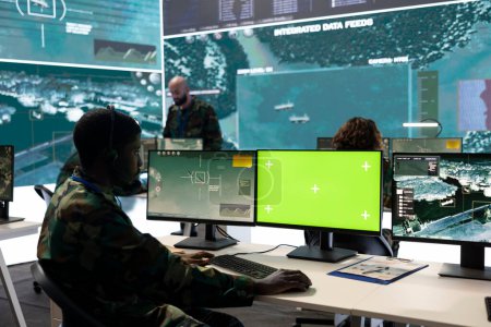Army personnel monitors isolated green screen and surveillance footage, gathering important battlefield information. Trooper examines CCTV reconnaissance imagery to support soldiers.