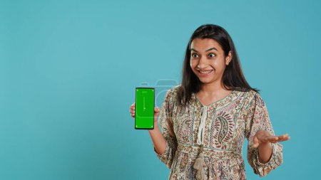 Tech Content Creator macht Influencer Marketing mit Green Screen Smartphone, isoliert über Studiohintergrund. Indische Frau hält leere Kopierraum-Handy-Attrappe, macht Rezension, Kamera A