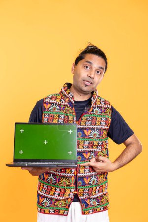 Portrait of tech professional pointing finger towards green screen laptop, isolated over studio backdrop. Content creator doing technology reviews, presenting mockup notebook