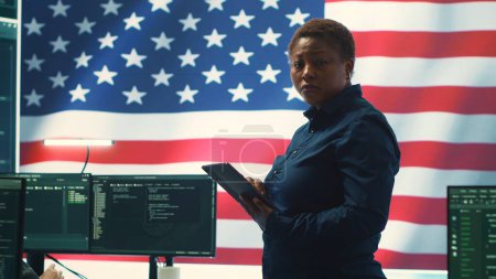 Spécialistes de la cybersécurité dans un bureau de haute technologie avec le drapeau américain, se concentrant sur le cyber-renseignement et les opérations de réseau sécurisé. Fonctionne sur la sécurité de l'information et la détection des logiciels malveillants. Caméra A.