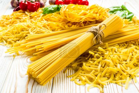 Téléchargez les photos : Spaghettis crus des variétés de blé léger tomates et légumes verts sur une table en bois - en image libre de droit