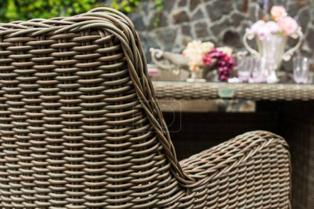 Photo for Armchair with wicker seat and dining table, outdoor furniture against stone wall background - Royalty Free Image