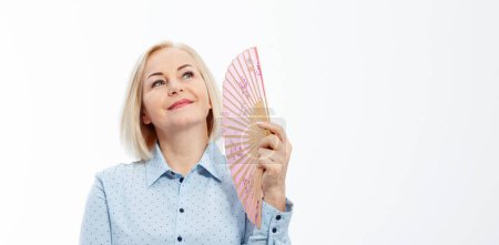 Beautiful middle aged woman with menopause blowing by fan. Hormone replacement therapy and mature woman healthcare. Mid age happy women lifestyle. Senior woman isolated on grey background