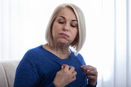 A woman in an uncomfortable position due to the discomfort of menopausal hot flushes. Mature woman experiencing hot flush from menopause at home