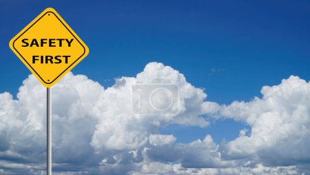 yellow safety first sign with a cloud blue sky in the background