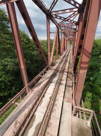 Téléchargez les photos : Les rails des voies ferrées s'étirent au loin, longeant le pont dans une végétation dense et estivale - en image libre de droit
