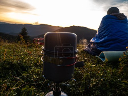 Foto de Un turista envuelto en una manta se sienta en la hierba y observa el amanecer. - Imagen libre de derechos