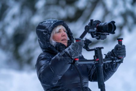 A woman in a winter jacket holds a camera with a stabilizer using a two-handed grip