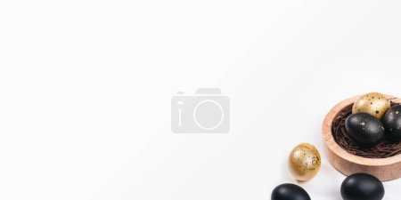 Foto de Huevos pintados de oro y negro sobre fondo blanco. Sobre el nido que contiene huevo. Concepto mínimo de Pascua con espacio de copia para texto. - Imagen libre de derechos