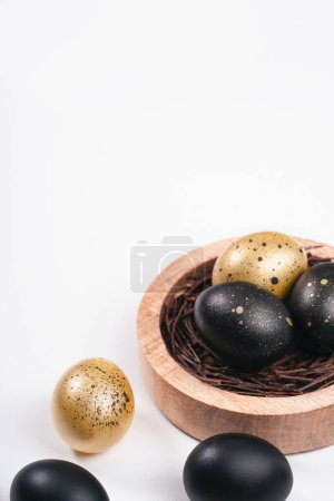 Foto de Huevos pintados de oro y negro sobre fondo blanco. Sobre el nido que contiene huevo. Concepto mínimo de Pascua con espacio de copia para texto. - Imagen libre de derechos