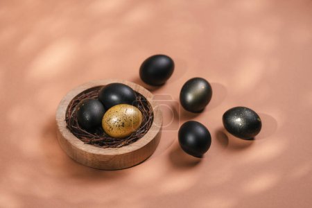 Foto de Huevos pintados de negro y oro sobre fondo biege. Nido que contiene tres huevos. Concepto mínimo de Pascua con espacio de copia para texto. - Imagen libre de derechos