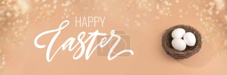 Photo for Easter concept with Happy Easter lettering. Eggs on a beige background. Nest containing three white egg. - Royalty Free Image