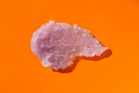Téléchargez les photos : Sugar body scrub texture on orange background. Cosmetic smear. Appearance of the texture of the lilac swatch. Natural skincare products. Beauty concept for face and body care. - en image libre de droit