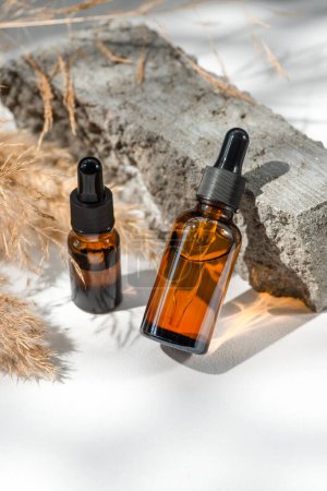 Photo for Amber glass droppers with black lid and dry plant. Bottles on grey concrete podium for product presentation. Skincare cosmetic with wildflowers. Beauty concept - Royalty Free Image