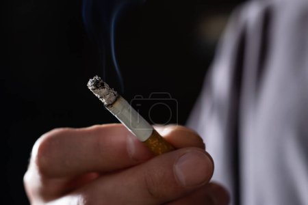 Téléchargez les photos : Gros plan homme main cigarette fumeur sur fond noir - en image libre de droit