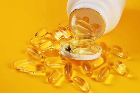 Foto de Cápsulas de aceite de pescado con omega 3 y vitamina D en una botella de color amarillo. - Imagen libre de derechos