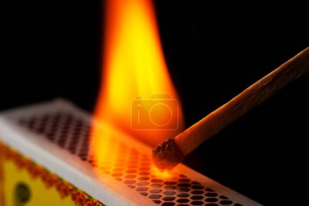 A matchstick lights after it is struck agains the flint surface of a match box. Everything is real, no flame filters