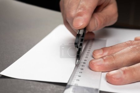 Foto de Hombre corta papel con un cuchillo de papelería y regla de cerca. - Imagen libre de derechos