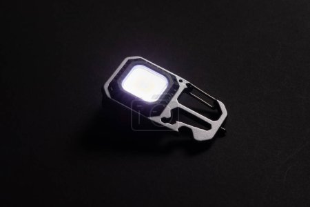 LED Flashlight Keychain and a beam of light in darkness. A modern led lamp with bright projection on dark table