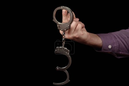 Handcuffs on Hand close up with Middle Finger on dark background.