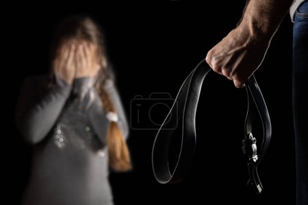 Photo for The girl hiding from her abusive stepfather. The concept of raising children through domestic violence. Punishment for a crime with a belt. The problem of child abuse. - Royalty Free Image