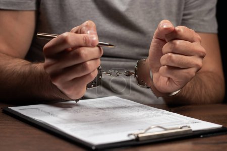 Tax evasion, crime and fraud concept. Man in handcuffs filling out tax form Income tax return documents and handcuffs