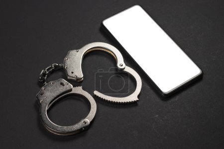 Phone in the Handcuffs on the dark Background close up. Mockup.