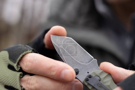 Hand in tactical glove, holding folding knife, close up.