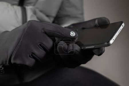 Hands in black thermal gloves hold and using smartphone in winter.