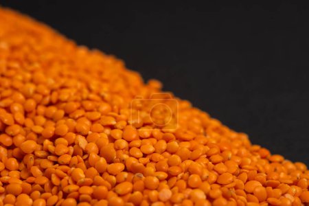 Pile of red lentils on dark background. Dry grains of red lentils. Orange lentils on a dark. Heap of orange lentils.