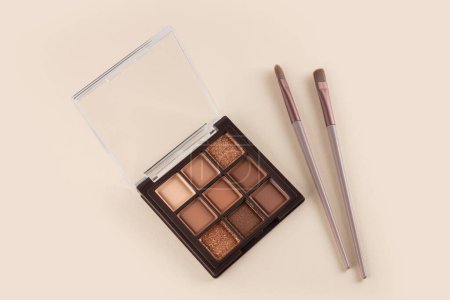 Make-up palette and brush on beige background. Professional multicolor eye shadow make-up palette. Cosmetic products.