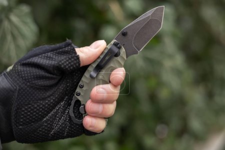 Hand in tactical glove, holding folding knife