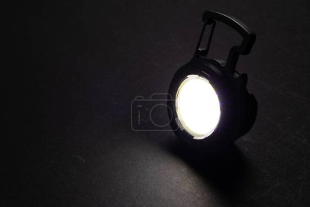Lampe de poche LED Porte-clés et un faisceau de lumière dans l'obscurité. Une lampe LED moderne avec projection lumineuse sur table noire