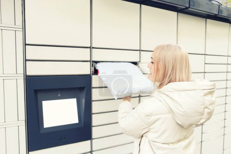 Photo for Blonde woman put the parcel in the self-service mail terminal. Parcel delivery machine. - Royalty Free Image